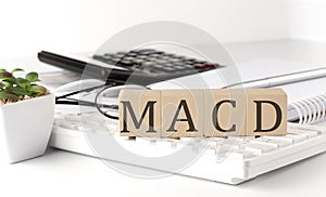MACD - Moving Average Convergence Divergence written on a wooden cube on keyboard with office tools