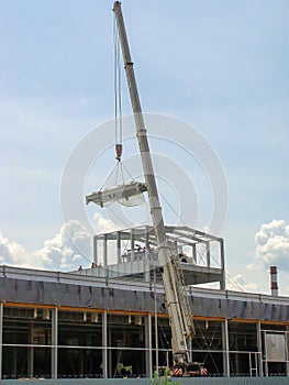 A machine crane with a high boom feeds refrigeration equipment suspended on cables to the roof