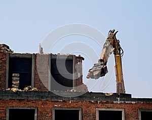 Machine destroying building walls on demolishion site.