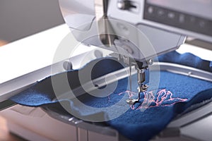Machine head and embroidery hoop of a modern sewing machine that stitches a magnolia with pink yarn on classic blue boiled wool