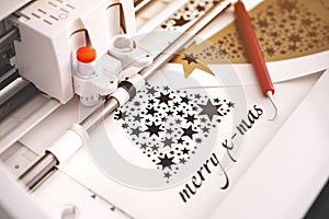 machine head of plotting machine with adjustable blade cuts christmas sticker with lettering from black adhesive vinyl.