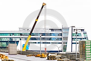 Machine lifting crane industrial equipment at a construction site on the background of a new, modern facade of an urban building