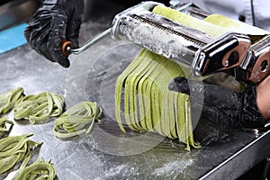 Machine for making pasta. Pasta dough with spinach. Unrecognizable person. Only hands in protective gloves