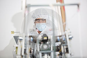 Machine staff, mask production department. Engineer wearing protective suit Inspecting quality of masks. machine production