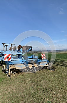 Machinery, equipment for plowing the ground, blue soil stands on green grass against the background of a blue sky. Close-up