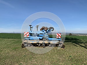 Machinery, equipment for plowing the ground, blue soil stands on green grass against the background of a blue sky. Close-up.