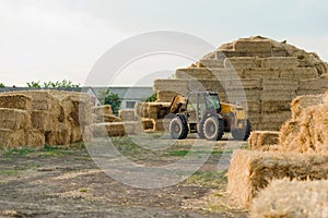 Machinery stacking hay bales in farm field. Tractor Storing Bails Of Hay