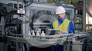 Machinery transporting plastic vessels is being inspected by a male worker