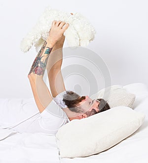 Macho with beard and mustache relaxing with plush toy after nap. Childhood memories concept. Man laying on bed and holds