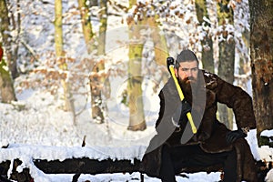 Macho with beard and mustache sits in forest holding axe
