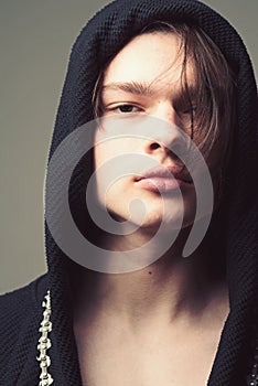 Macho in black bathrobe with hood, close up. Guy on confident face in black hood, grey background. Masculinity concept