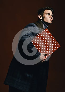 Macho carries present on red background. Guy with serious face
