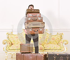 Macho elegant on surprised face carries pile of vintage suitcases. Man with beard and mustache wearing classic suit