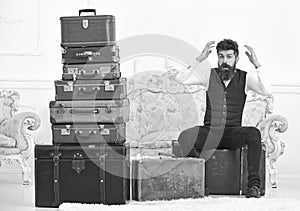Macho elegant on surprised face sits shocked near pile of vintage suitcase. Luggage and relocation concept. Man, butler