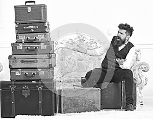 Macho elegant on surprised face sits shocked near pile of vintage suitcase. Luggage and travelling concept. Man, butler