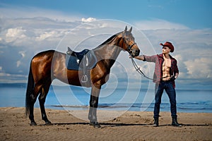 Macho man handsome cowboy and horse on the background of sky and water. photo
