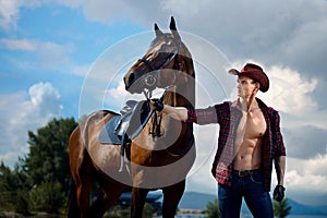 Macho man handsome cowboy and horse on the background of sky and water. photo