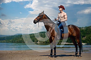 Macho man handsome cowboy riding on a horse on the background of sky and water.