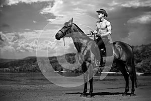 Macho man handsome cowboy riding on a horse on the background of sky and water. photo