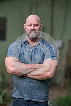 Macho tough guy posing with arms crossed. Man is bald with a full beard