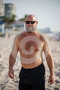 Macho tough guy walking on the beach. Man is wearing sunglasses and no shirt
