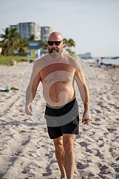 Macho tough guy walking on the beach. Man is wearing sunglasses and no shirt