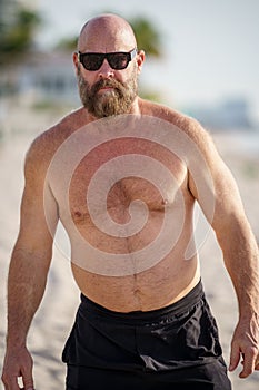 Macho tough guy walking on the beach. Man is wearing sunglasses and no shirt