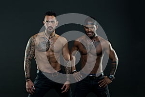 Machos with muscular tattooed torsos look attractive, dark background. Athletes on confident faces with nude muscular photo