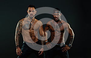 Machos with muscular tattooed torsos look attractive, dark background. Athletes on confident faces with nude muscular photo