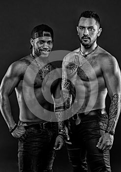 Machos with muscular tattooed torsos look attractive, dark background. Guys sportsmen with muscular torsos.