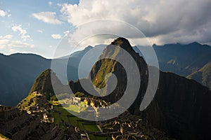 Machu Picchu illuminated by the warm sunset light. Wide angle view from the terraces above with scenic sky and sun burst. Dreamlik