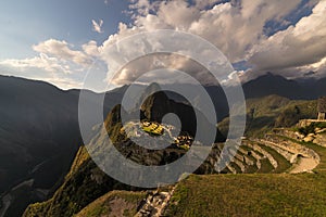 Machu Picchu illuminated by the warm sunset light. Wide angle view from the terraces above with scenic sky and sun burst. Dreamlik