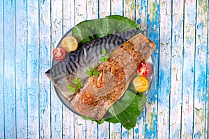Mackerel fillet salted with spices served with fresh vegetable salad on the plate on blue wooden table.