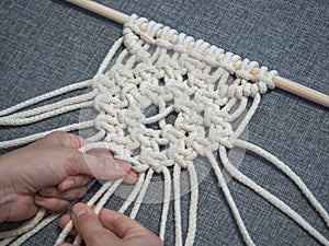 Macrame. Girl weaves macrame. White thread, female hand, grey background, close-up photo