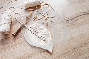 Macrame leaf  in natural color and thread windings lying on a wooden table. Cotton rope decor macrame to make your room more cozy