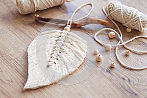 Macrame leaf  in natural color and thread windings lying on a wooden table. Cotton rope decor macrame to make your room more cozy