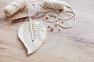 Macrame leaf  in natural color and thread windings lying on a wooden table. Cotton rope decor macrame to make your room more cozy