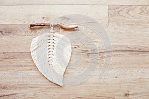 Macrame leaf  in natural color and thread windings lying on a wooden table. Cotton rope decor macrame to make your room more cozy