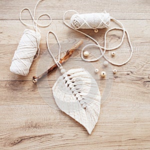 Macrame leaf  in natural color and thread windings lying on a wooden table. Cotton rope decor macrame to make your room more cozy