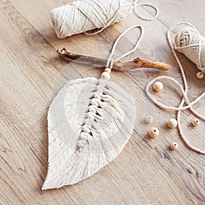 Macrame leaf  in natural color and thread windings lying on a wooden table. Cotton rope decor macrame to make your room more cozy