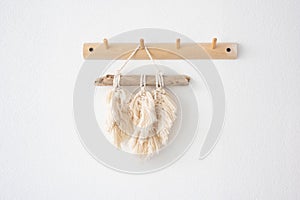 macrame panels hang on a wooden hook on a light wall.