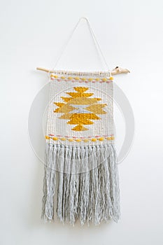 Macrame tapestry with yellow-colored patten hanging on the wall