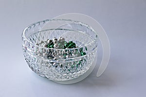 Macro abstract background of a beautiful diamond faceted lead crystal glass bowl containing green and silver metallic beads