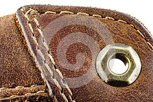 Macro background made of brown natural leather with white stitches all around, visible metal leathercraft eyelet.