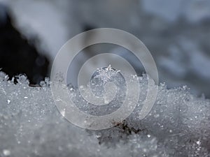 Macro of the beautiful, geometrical snowflake reflecting light in crystals on snow surface. Detailed shot of a snowflake