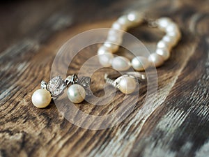 Macro of beautiful pearl earrings and Bride ring on wooden background.