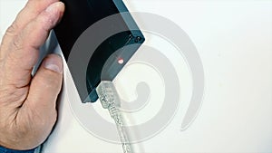 Macro of the black hard drive on the table and old man hand putting a white cable in it. Shot. Close up with plug usb