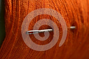 sewing needle on orange bobbin thread.