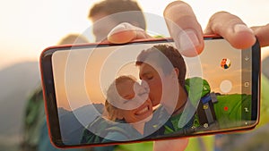 MACRO: Cheerful man takes a selfie of him kissing girlfriend on cheek at sunset.