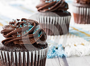 A macro close up of a chocolate cupcake with chocolate frosting and other cupcakes in soft focus in behind.